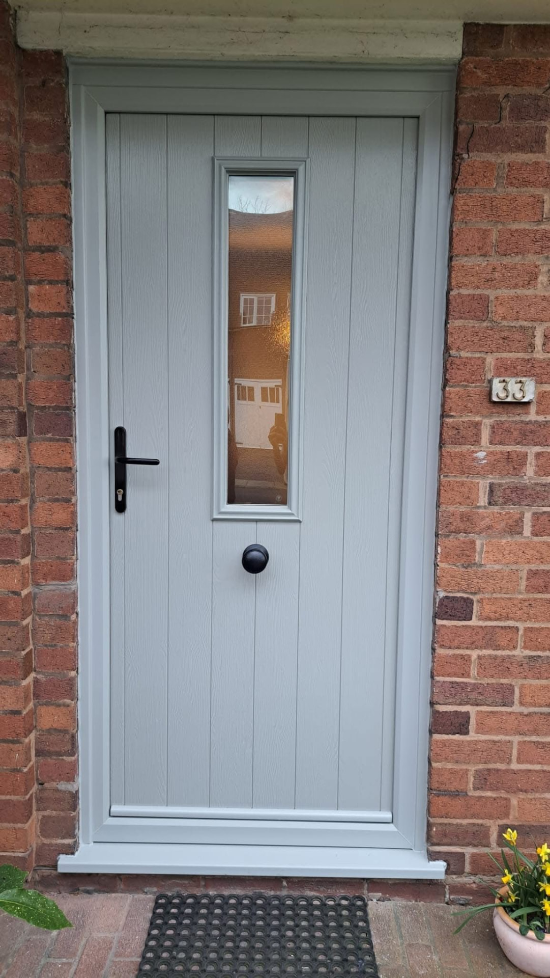 Light grey composite door with vertical frosted window and black ring knocker
