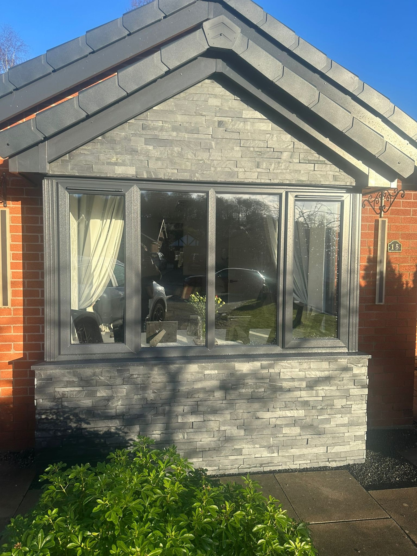 Grey uPVC porch infill with stone cladding and anthracite window frames on a brick bungalow
